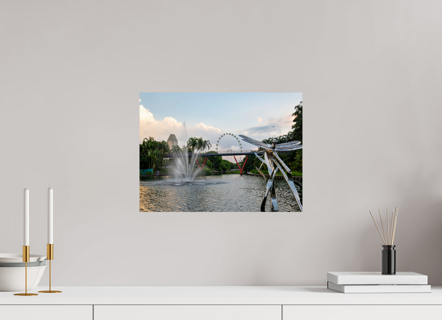 Framed photograph of a park scene with a lake, fountain, and Ferris wheel on a wall above a white shelf.