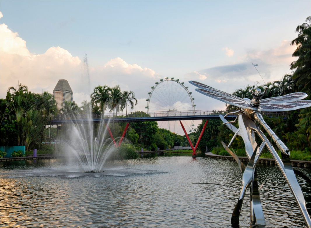 Dragonfly sculpture by a fountain with a Ferris wheel and bridge in the background